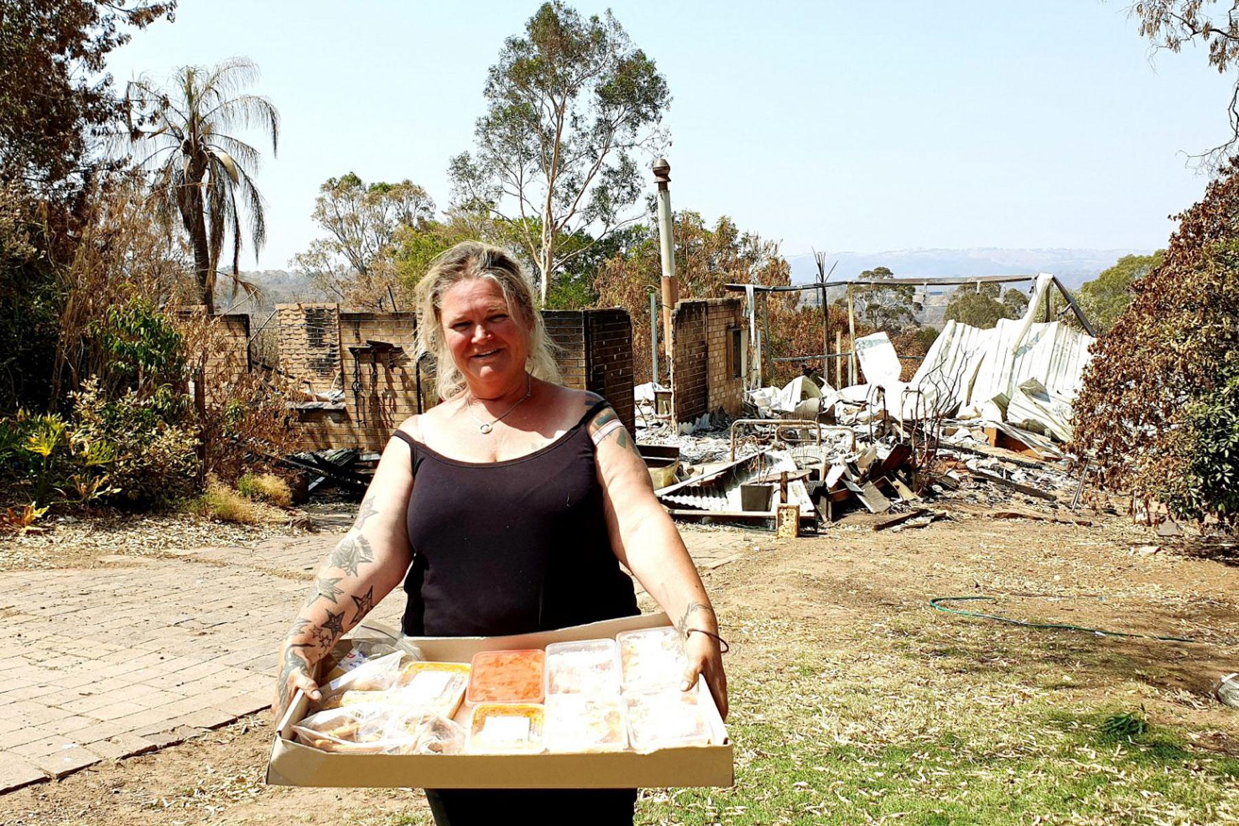 Sue Cutting, Pflegemutter von sieben Kindern, steht vor den Ruinen ihres Hauses, freut sich jedoch über die Nahrungsmittelhilfe, die ihr Freiwille der Adelaide Hills-Gemeinde vorbeibrachten. Fotos LCA