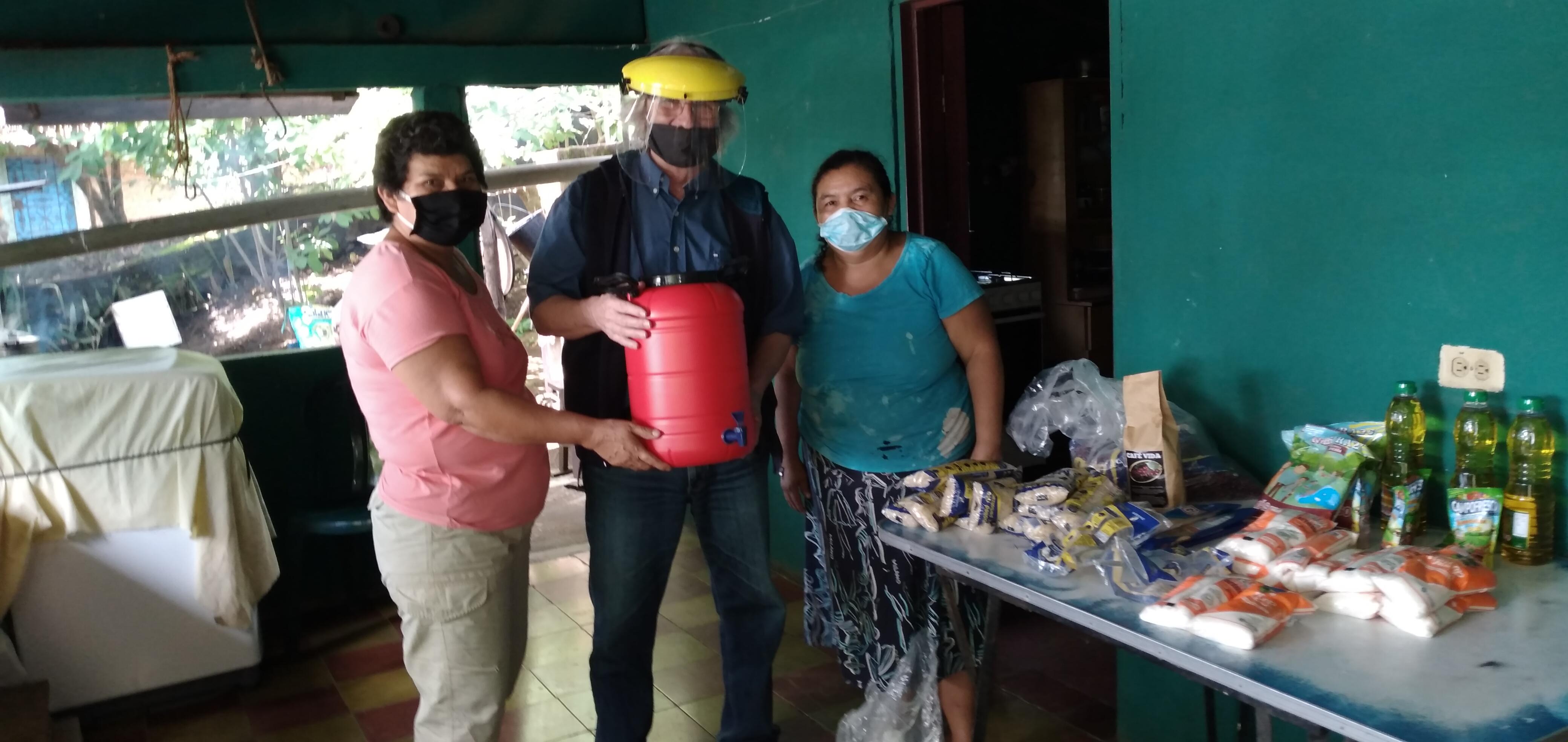 Hans-Jürgen Johnke (mitte), Mission EineWelt-Mitarbeiter in El Salvador übergibt Lebensmittel und einen Kanister zur Handreinigung an Gemeindemitglieder in El Volcan. Foto: MEW