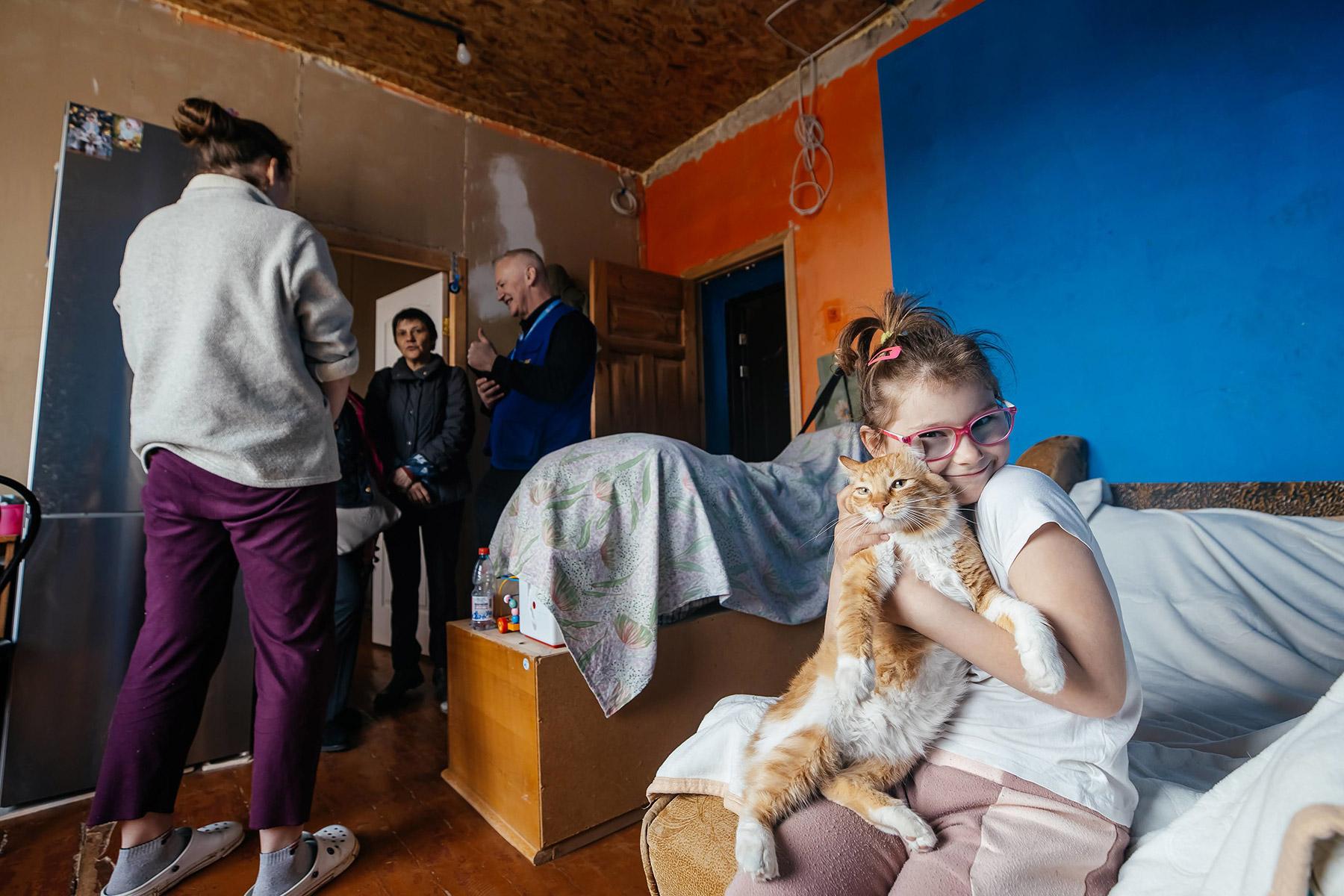 A girl holds her cat while an LWF team discusses reconstruction needs with her mother. Photo: LWF/ Anantoliy Nazarenko