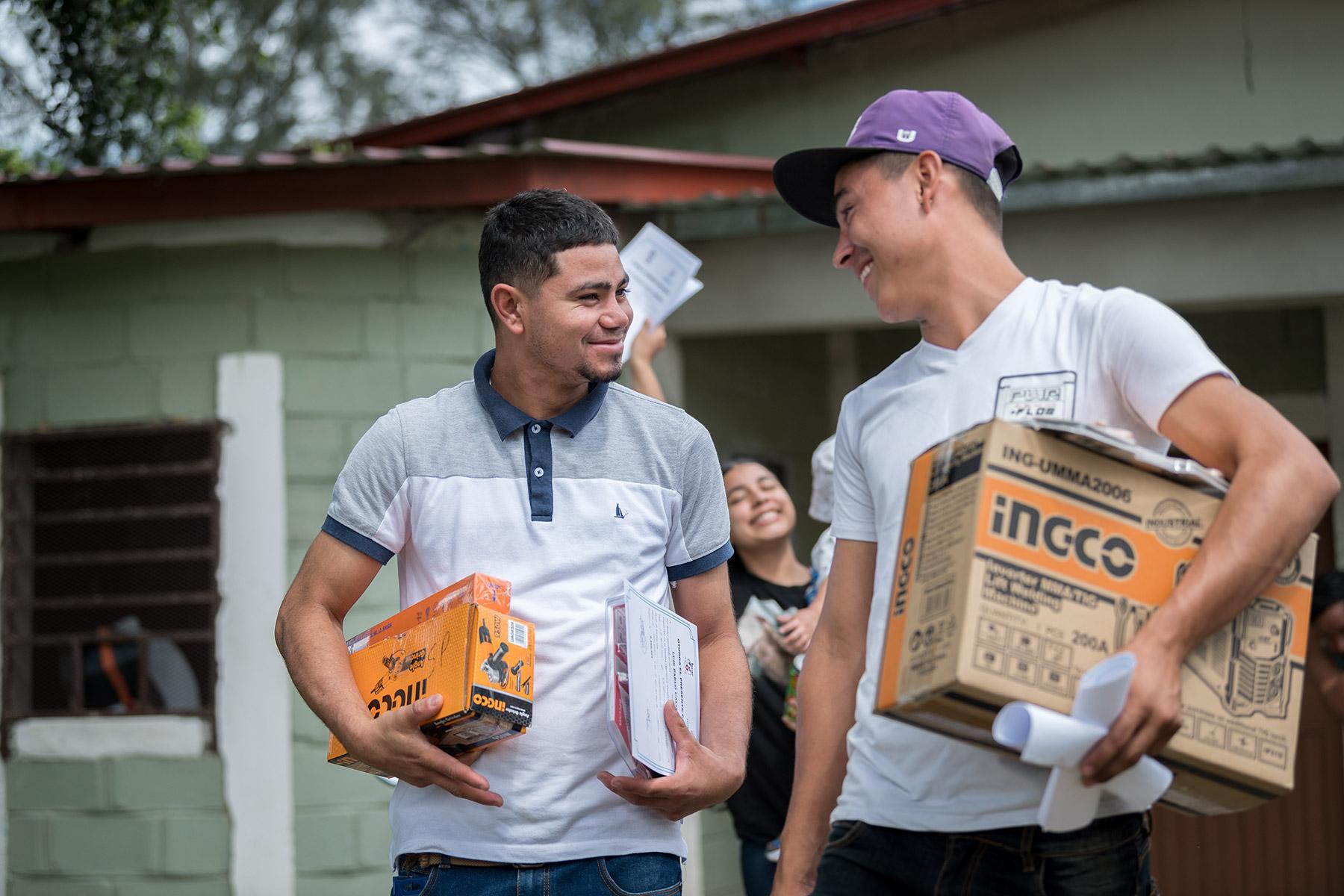 26 October 2023 El Guante, Cedros, Honduras: Luis Pablo Calix (left) and Immey Janiel Gonzales (right) – two young returned migrants receiving support from the Lutheran World Federation World Service program – carry boxes they have picked up from a community center in El Guante, Cedros. Photo: LWF/A. Hillert