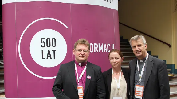 Vor dem neuen Reformationslogo der polnischen lutherischen Kirche: Bischof Jerzy Samiec, LWB-Ratsmitglied Iwona Baraniec und LWB-Generalsekretär Martin Junge [am Rande der Tagung der Kirchenleitenden in der Region Mittel- und Osteuropa vom 3. bis 4. Juli 2014 in Breslau (Polen)]. Foto: LWB/Florian Hübner