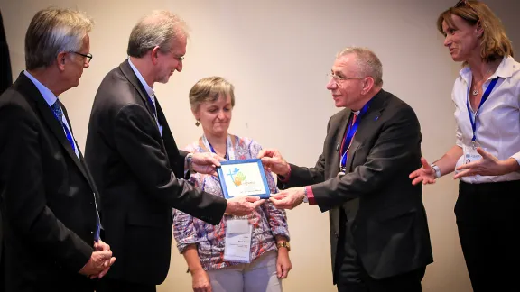 Marcia Blasi, Evangelical Church of the Lutheran Confession in Brazil, LWF General Secretary Martin Junge and Regional Program Coordinator Anne Caroline Tevoy look on as Bishop Munib Younan presents a decorative tile of the LWF Assembly logo to the Rev. Dr. Nestor Paulo Friedrich, Evangelical Church of the Lutheran Confession in Brazil. The Brazilian church made a gift to the AVH Hospital and the tile is a token of thanks. Photo: LWF/Johanan Celine Valeriano