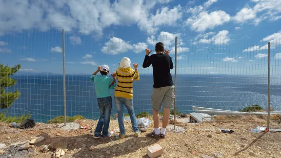 Syrian refugee children at a fence facing the Aegean Sea coast, Greece. Photo: ACT/ Paul Jeffrey