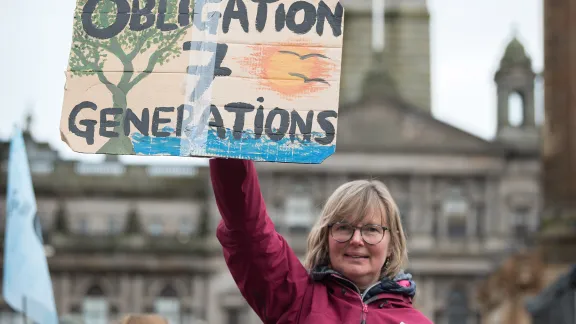 Kathrin Hall holds a sign at an interfaith vigil held at George Square on the opening day of COP26 in Glasgow, Scotland. Photo: LWF/Albin Hillert