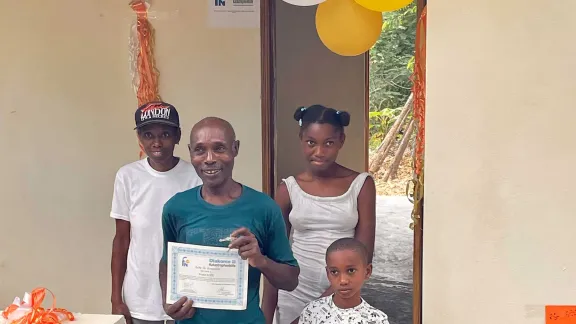 The Family Pradel, community of Fon Kochin, Grand Anse, received the key to their new house, built by the Joint Office as part of the response to the August 2021 earthquake. Also pictured is the shelter they have been living in for the past two years. Photo: LWF/ M. French