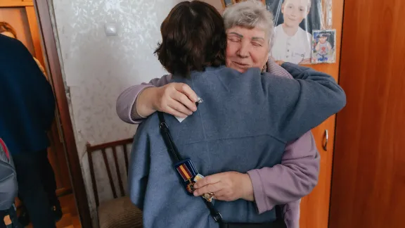 Maria Ivaninvna from Kharkiv hugs LWF General Secretary Rev. Dr Anne Burghardt on the solidarity visit on 14 May 2024. Ivanivna's apartment was hit by a missile in 2022 and rehabiliated by LWF. Behind her are the pictures of her sons, who are fighting in the army, and her grandson. Photo: LWF/ Anatolyi Nazarenko