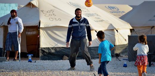 A man plays football with his children in the Zaatari Refugee Camp, Jordan, while another man, wounded in fighting in Syria, looks on. Photo: Paul Jeffrey/ACT